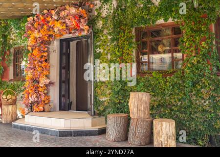 La porte d'entrée du café. Il y a des souches d'arbres devant l'entrée. Il y a des plantes grimpantes sur les murs. Il y a des décorations d'automne Banque D'Images