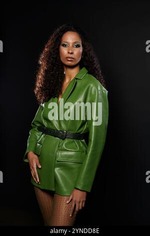 Une femme confiante affiche une tenue verte vibrante avec une forte expression dans un studio élégant. Banque D'Images