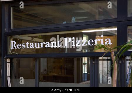 Un panneau de restaurant-pizzeria moderne, orné de lettres blanches audacieuses, est affiché sur une fenêtre en verre. L'intérieur du restaurant est partiellement visible throu Banque D'Images