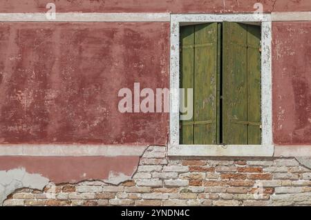 Vieux mur avec surface rouge altérée et volets verts, briques apparentes ci-dessous, Burano, Venise, Italie, Europe Banque D'Images