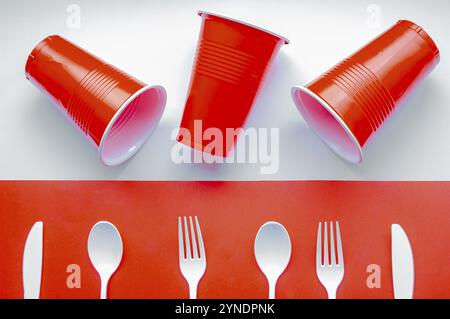 Couverts en plastique blanc à usage unique et verre en plastique rouge sur fond rouge et blanc. Concept : interdiction du plastique à usage unique Banque D'Images