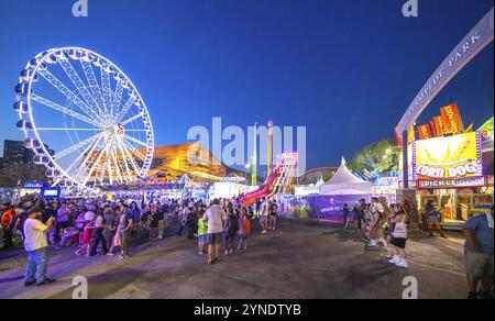 Calgary, Alberta, Canada. 22 juillet 2024. Une soirée animée au Stampede Park, avec une grande roue éclairée, un toboggan coloré et une corneille animée Banque D'Images