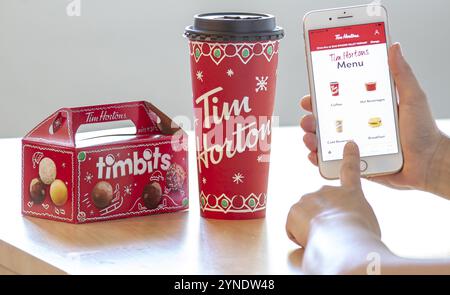 Calgary (Alberta). Canada 28 Déc 2019. Une personne titulaire d'un iPhone à l'aide de l'app Tim Hortons avec un café et une boîte de Tim Bits pendant Noël. Tim H Banque D'Images