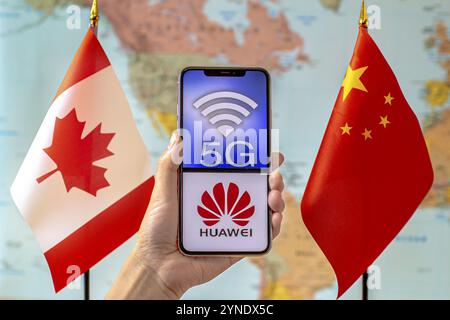 Calgary, Alberta, Canada. 8 septembre 2020. Personne tenant un iPhone avec un logo 5G et Huawei à l'écran à côté d'un drapeau du Canada et de la Chine sur un monde Banque D'Images