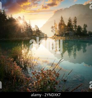 Lac idyllique au lever du soleil, un paysage pittoresque à Eibsee, en Allemagne, avec des montagnes et la lumière dorée du soleil venant derrière les arbres et illuminant Banque D'Images