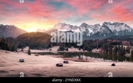 Paysage magique de lever de soleil avec des montagnes, des nuages illuminés, un lac pittoresque et des bois sur les collines dans les Alpes, prairie gelée et cabanes. Belle nature i Banque D'Images