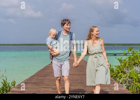Maman, papa et leur bébé fils explorant la jetée en bois au-dessus des eaux turquoises du lac Bacalar, au Mexique. Concept de destination de voyage tropical paisible Banque D'Images