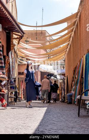 Jeune femme aux cheveux foncés en costume bleu marine et chapeau blanc debout dans une rue couverte à Marrakech, Maroc Banque D'Images