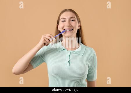 Fille avec des accolades nettoyant les dents sur fond beige Banque D'Images