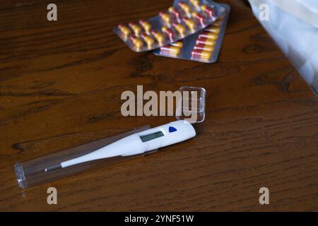 Thermomètre numérique dans un étui en plastique sur une table en bois avec des blisters de capsules Banque D'Images