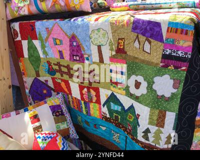 Une courtepointe présente des couleurs vives et des motifs ludiques représentant de charmantes maisons, arbres et animaux de la ferme. Les pièces de tissu fabriquées à la main créent un a animé Banque D'Images