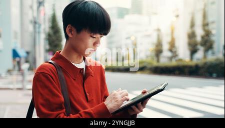 Ville, défilement et homme dans la rue avec tablette, trajet matinal ou recherche de navigation routière sur le passage à pied. Étudiant en milieu urbain, voyage et université japonaise sur Banque D'Images
