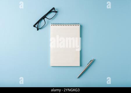 Vue de dessus du cahier, des lunettes et du stylo à bille sur fond bleu Banque D'Images