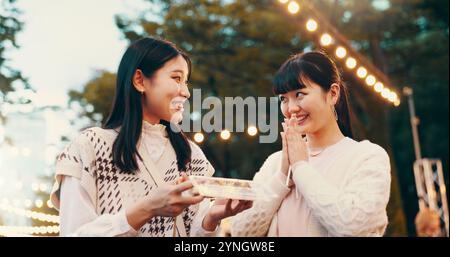 Femmes en plein air, asiatiques et heureuses de bonbons, de partage et de collation pour les amis en ville, gratitude et route. Gâterie, déplacements et bonbons pour la célébration de Banque D'Images