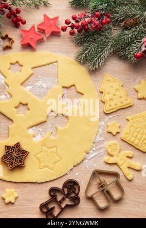 La pâte déroulée est en cours de préparation pour les biscuits de noël, avec diverses formes festives comme des maisons, des arbres, des étoiles et des flocons de neige Banque D'Images