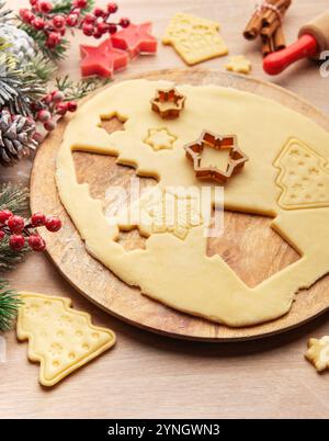 La pâte déroulée est en cours de préparation pour les biscuits de noël, avec diverses formes festives comme des maisons, des arbres, des étoiles et des flocons de neige Banque D'Images