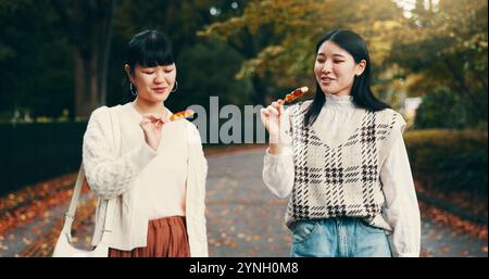 Parc, femmes asiatiques et heureux avec bonbons, voyage et collation pour les amis avec dango, étudiants et la route. Plein air, déplacements et bonbons pour la célébration de Banque D'Images