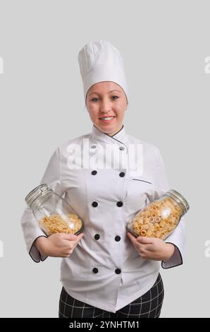 Femme chef tenant deux bocaux en verre remplis de différents types de pâtes, promouvant la cuisine italienne Banque D'Images