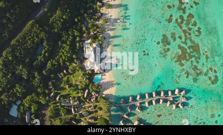 Complexe de bungalows de luxe haut de gamme sur une île tropicale, une forêt de cocotiers verte vibrante, un lagon d'eau turquoise cristallin. Villas sur l'eau huttes sur la plage de sable. Voyage exotique escapade de vacances, aérien Banque D'Images