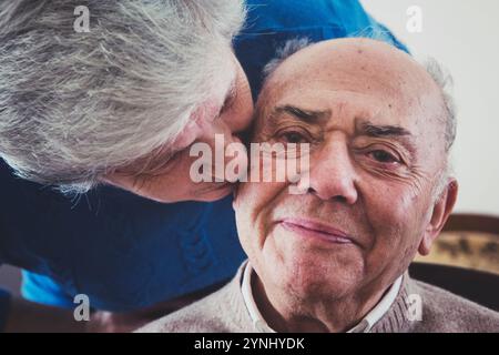 Un couple d'aînés aimant profite d'un doux moment ensemble à la maison, avec un partenaire embrassant affectueusement la joue de l'autre, entouré d'une atmosphère chaleureuse Banque D'Images