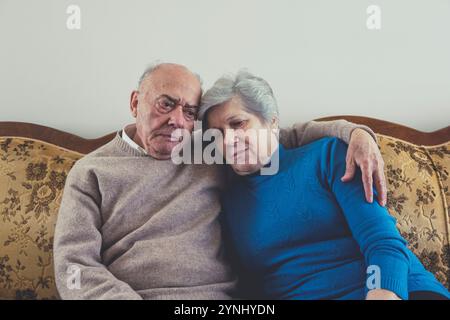 Un couple âgé est assis étroitement ensemble sur un canapé confortable, partageant un moment émotionnel. Ils affichent l'amour et l'affection dans leur env. De la maison détendue Banque D'Images