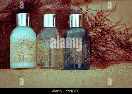 Bouteilles en plastique, récipients avec des cosmétiques écologiques - shampooing, gel douche, lotion pour le corps pour les soins de la peau du visage - sur la côte sablonneuse parmi les algues rouges. NAT Banque D'Images