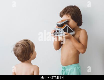 Deux jeunes garçons se livrent à des jeux imaginatifs avec un appareil photo vintage à l'intérieur. Un enfant fait semblant de prendre des photos tandis que l'autre regarde curieusement. T Banque D'Images