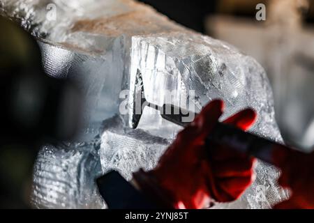 Oberhausen, Allemagne. 26 novembre 2024. Un artiste façonne un bloc de glace avec un grattoir à glace pointu lors d'une exposition de sculptures sur glace et neige, Centro Oberhausen. Crédit : Christoph Reichwein/dpa/Alamy Live News Banque D'Images