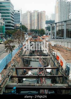 Chantier de construction urbaine avec tuyaux de service public exposés, appartements de grande hauteur et bâtiments modernes illustrant le développement de l'infrastructure. Banque D'Images