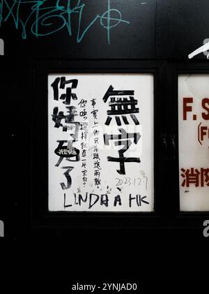 Signalisation urbaine avec calligraphie chinoise manuscrite et encre noire sur un fond blanc encadré dans une allée de Hong Kong Banque D'Images