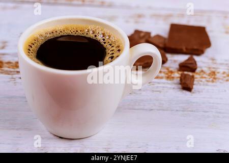 Café chaud dans une tasse blanche à côté de morceaux de chocolat noir sur une surface en bois rustique Banque D'Images