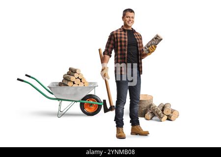 Homme avec une brouette et du bois de chauffage souriant et tenant une hache isolée sur fond blanc Banque D'Images