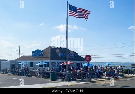 Gilgo Beach, New York, États-Unis - août 2023 : les clients apprécient la nourriture et les boissons à l'extérieur au Gilgo Beach Bar pendant que le drapeau américain agite dans la brise. Banque D'Images