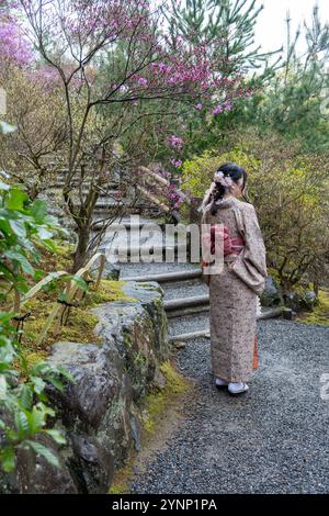 Jeune femme en robe traditionnelle japonaise marchant dans un jardin, vue arrière. Arbres en fleurs, printemps au Japon. Banque D'Images