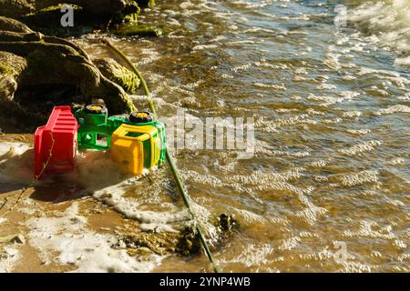 Les camions jouets aux couleurs vives reposent sur le rivage sablonneux, partiellement immergés dans les vagues scintillantes, avec la lumière douce du soleil se reflétant sur l'eau, créant Banque D'Images