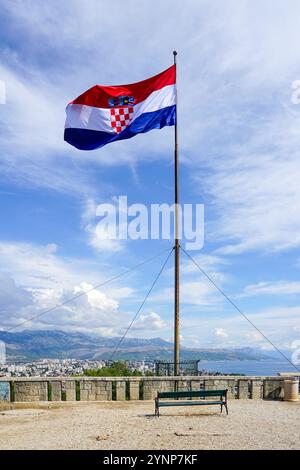 Un grand drapeau croate vole sur un haut mât sur une montagne au-dessus de la ville de Split, ciel bleu avec des nuages blancs Banque D'Images