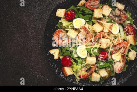 Salade César avec crevettes tigrées, salade de crevettes, feuilles de laitue, œufs de caille, tomates cerises, parmesan, sur assiette noire Banque D'Images