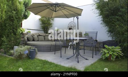 Terrasse de jardin avec salon et coin salon et parasol dans un coin du jardin avec un pin en colonne U. Banque D'Images