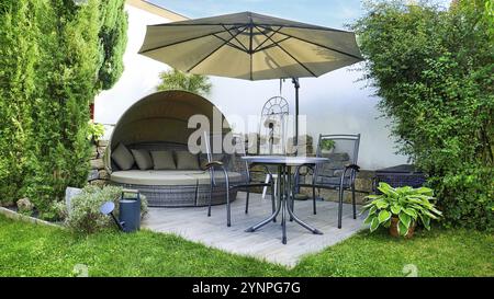 Terrasse de jardin avec salon et coin salon et parasol dans un coin jardin avec diverses plantes Banque D'Images