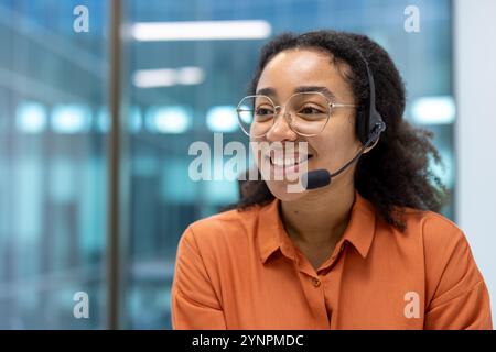 Agent d'assistance clientèle confiant portant un micro-casque/une oreillette souriante dans un bureau moderne. L'atmosphère professionnelle transmet la communication, le service et le succès au travail Banque D'Images