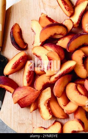 Pêches fraîchement tranchées disposées sur une planche à découper en bois, mettant en valeur leurs couleurs vives et leur texture juteuse. Banque D'Images