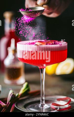 Une photo d'action de poudre de baies rose vif saupoudrée sur une boisson alcoolisée sophistiquée, avec un verre à cocktail à tige texturée Banque D'Images