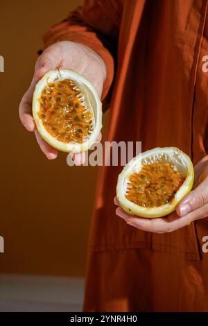 Main tenant des fruits de la passion fraîchement coupés (Passiflora edulis et Passiflora ligularis), révélant sa pulpe d'orange vibrante et juteuse remplie de graines brillantes Banque D'Images