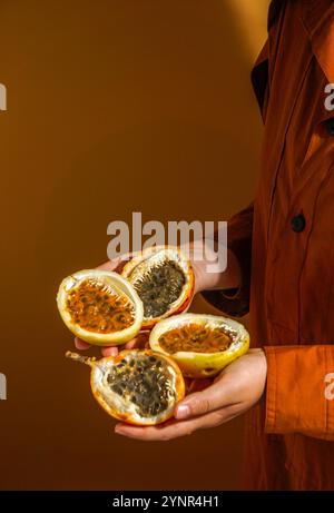 Main tenant des fruits de la passion fraîchement coupés (Passiflora edulis et Passiflora ligularis), révélant sa pulpe d'orange vibrante et juteuse remplie de graines brillantes Banque D'Images