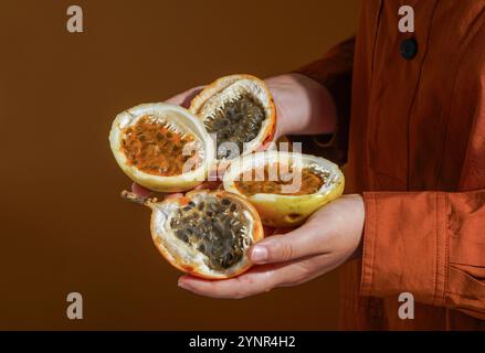 Main tenant des fruits de la passion fraîchement coupés (Passiflora edulis et Passiflora ligularis), révélant sa pulpe d'orange vibrante et juteuse remplie de graines brillantes Banque D'Images