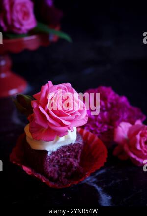 Red Velvet Cupcakes avec roses roses fleurs comestibles en gros plan. Banque D'Images