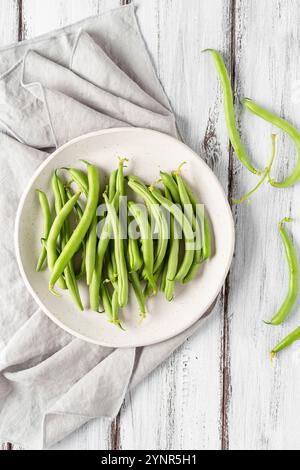 Haricots verts fraîchement cueillis, dans une assiette, sur une table en bois blanc. Vue de dessus. Banque D'Images