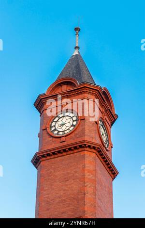 Tour d'horloge hydraulique victorienne en briques rouges historique avec un toit pointu contre un ciel bleu clair, présentant des détails architecturaux ornés Banque D'Images