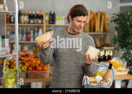 Homme avec panier choisissant le fromage emballé dans le marché rustique Banque D'Images