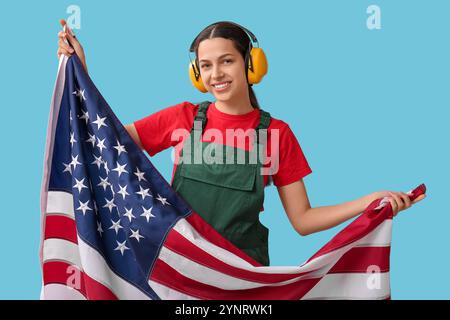 Ouvrière de la construction féminine avec des protections auditives et drapeau des États-Unis sur fond bleu Banque D'Images